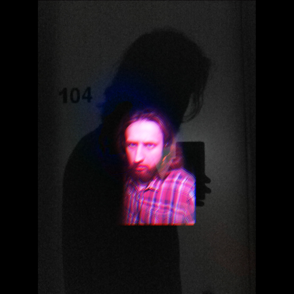 A dark self portrait lit in pink and blue, standing against a wall marked 104, with a large shadow behind.